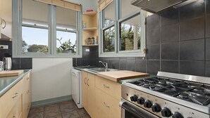 A modern kitchen with a gas stove, a sink, and wooden cabinets. - Fishermans Cottage - Queenscliff (QUEENSCLIFF)