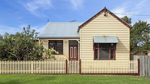A two-story house with a gabled roof, a picket fence, and a small porch. - Fishermans Cottage - Queenscliff (QUEENSCLIFF)
