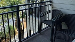 A balcony with a view of the beach, a chair, and a railing.