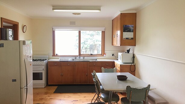 A compact kitchen with wooden cabinets, a white refrigerator, a stove, a microwave, and a window above the sink. - The Beach Shack - Queenscliff (Queenscliff)