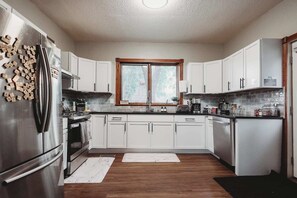 A modern kitchen with white cabinets, stainless steel appliances, a window, and a wooden floor.