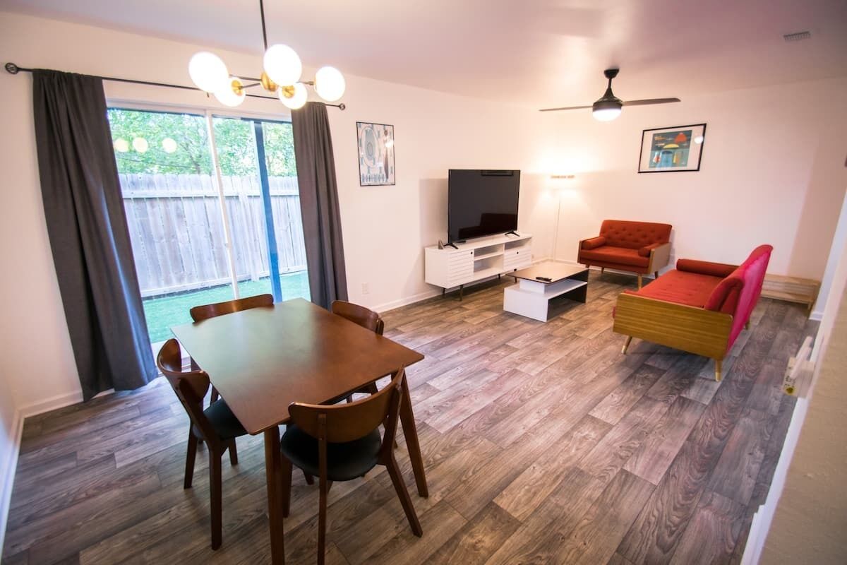 Ein Wohnzimmer mit einem Holzesstisch, Stühlen, einer Couch, einem Fernseher und einem Deckenventilator.