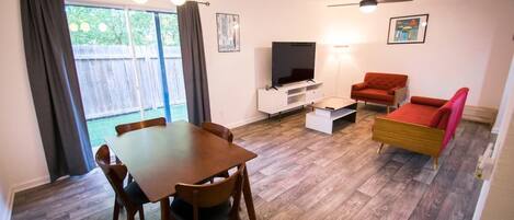 Ein Wohnzimmer mit einem Holzesstisch, Stühlen, einer Couch, einem Fernseher und einem Deckenventilator.