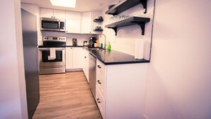 A compact kitchen with white cabinets, a black countertop, and a microwave. - Atomic Age (Austin)