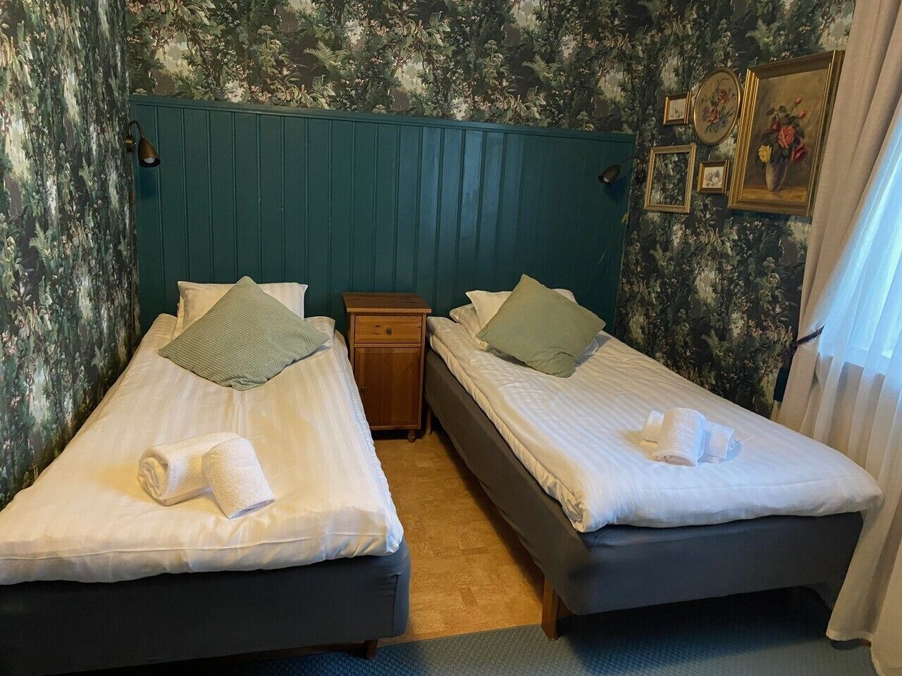 Ett hotellrum med två sängar, ett nattduksbord och en vägg med blommig tapet.