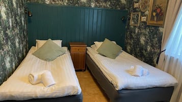 Ett hotellrum med två sängar, ett nattduksbord och en vägg med blommig tapet.