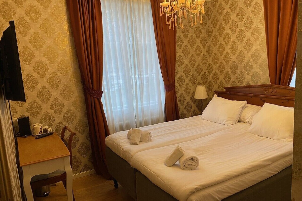 Ein Hotelzimmer mit Bett, Schreibtisch, Sessel, Fernseher und einer Chandelüster.