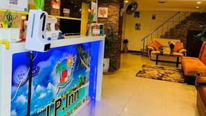 A reception desk with a tropical-themed design, a staircase, and a seating area with an orange sofa and a coffee table. - J P Inn Pattaya Boutique Hotel (Pattaya)