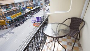 A balcony with a glass table and wicker chair, overlooking a busy street with shops and parked motorcycles. - J P Inn Pattaya Boutique Hotel (Pattaya)