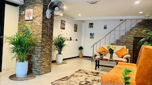 A modern living room with a stone accent wall, a sofa with orange cushions, and a glass coffee table. - J P Inn Pattaya Boutique Hotel (Pattaya)