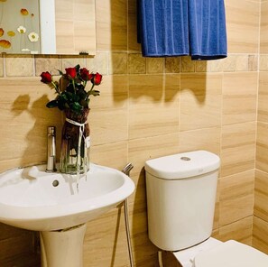 Une salle de bain avec un lavabo blanc, des toilettes et un vase contenant des roses rouges.