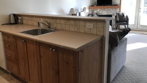 A kitchen with a double sink, wooden cabinets, a stone backsplash, and a television above the counter.