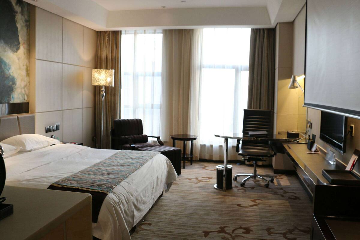 A hotel room with a large bed, a desk with a computer, a chair, a small table, and a TV.