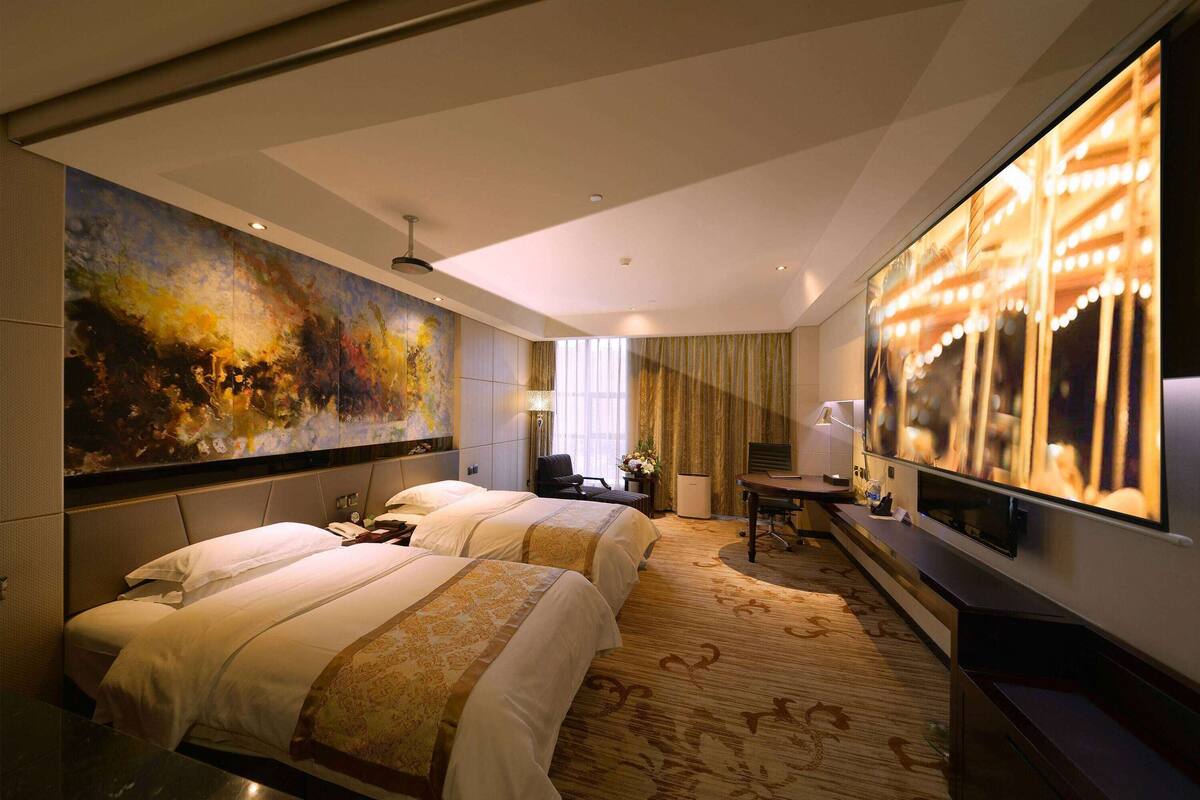 A hotel room with two beds, a large painting, a TV, and a desk with a lamp.