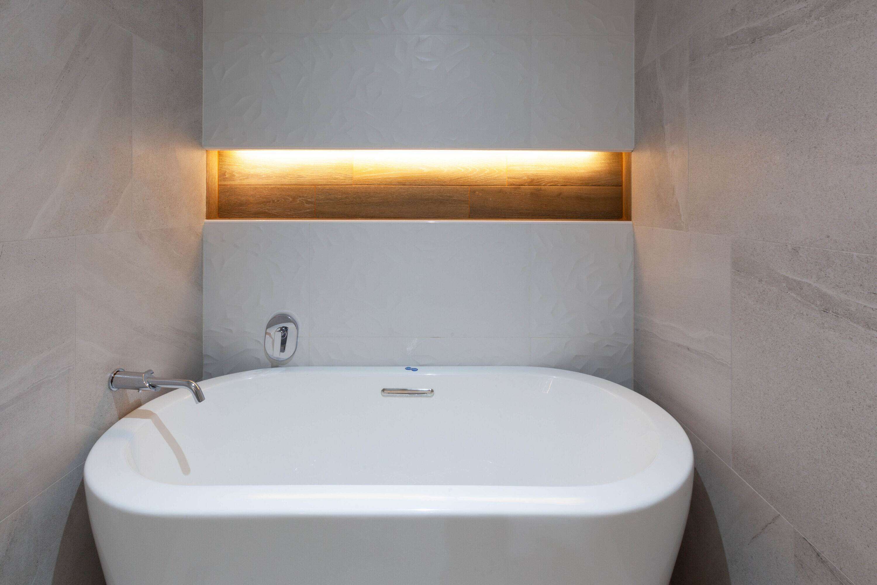 A modern bathroom with a freestanding bathtub, a wooden panel above the sink, and a wall-mounted faucet.