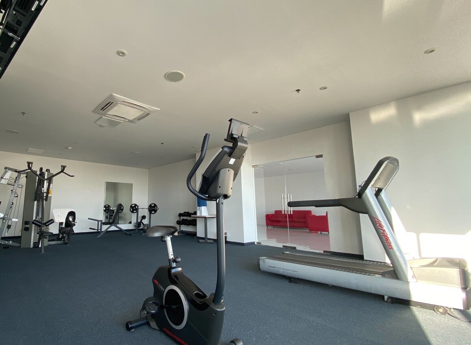 A gym with cardio equipment, weight machines, and a red couch in the background.
