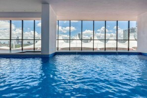 A swimming pool with a city view through large windows. - Wyndham Puebla Angelopolis (San Andrés Cholula)