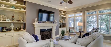 A living room with a fireplace, white sofas, a television, and decorative items on shelves.