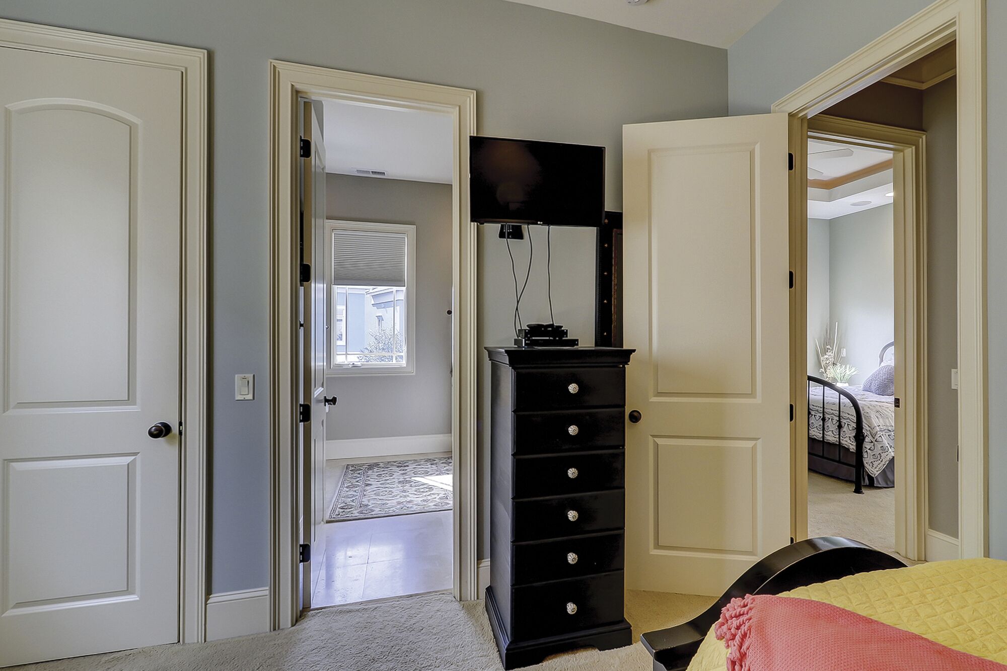 Een slaapkamer met een bed, een dressoir en een televisie. Er zijn deuren naar andere kamers.