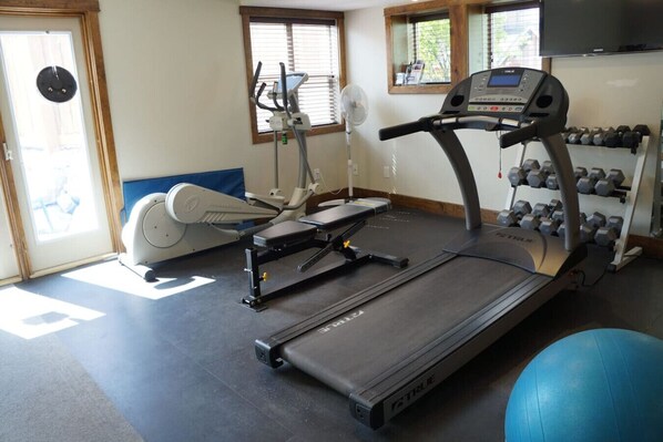 A gym with a treadmill, elliptical, and weight rack.