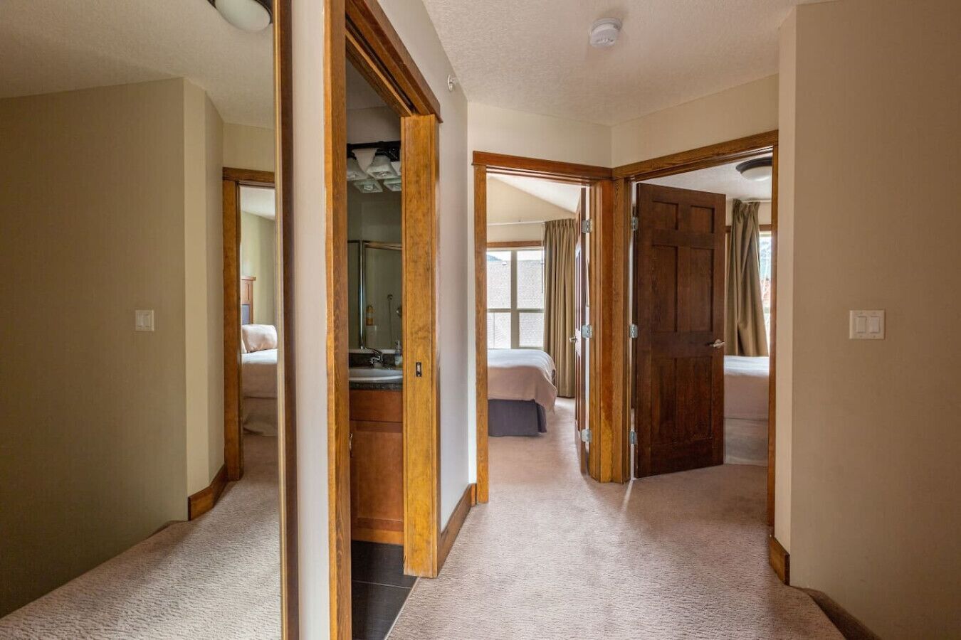 Un couloir mène à une chambre dotée d’une grande fenêtre, à une salle de bain avec un miroir et à une porte qui donne sur une autre pièce.