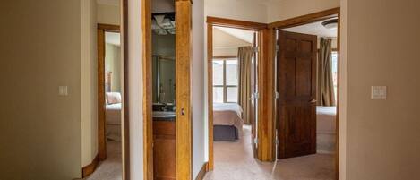 Un couloir mène à une chambre dotée d’une grande fenêtre, à une salle de bain avec un miroir et à une porte qui donne sur une autre pièce.