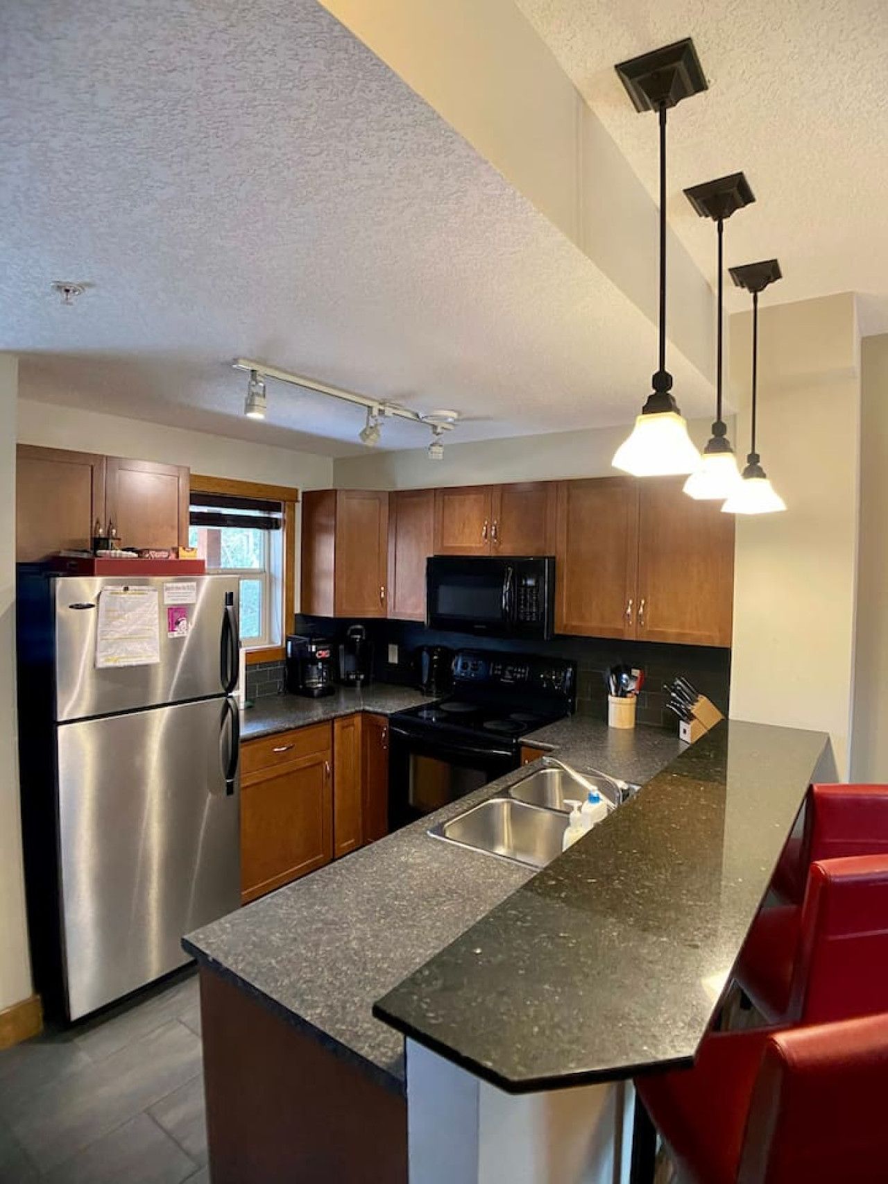 A modern kitchen with stainless steel appliances, wooden cabinets, a granite countertop, and pendant lighting.