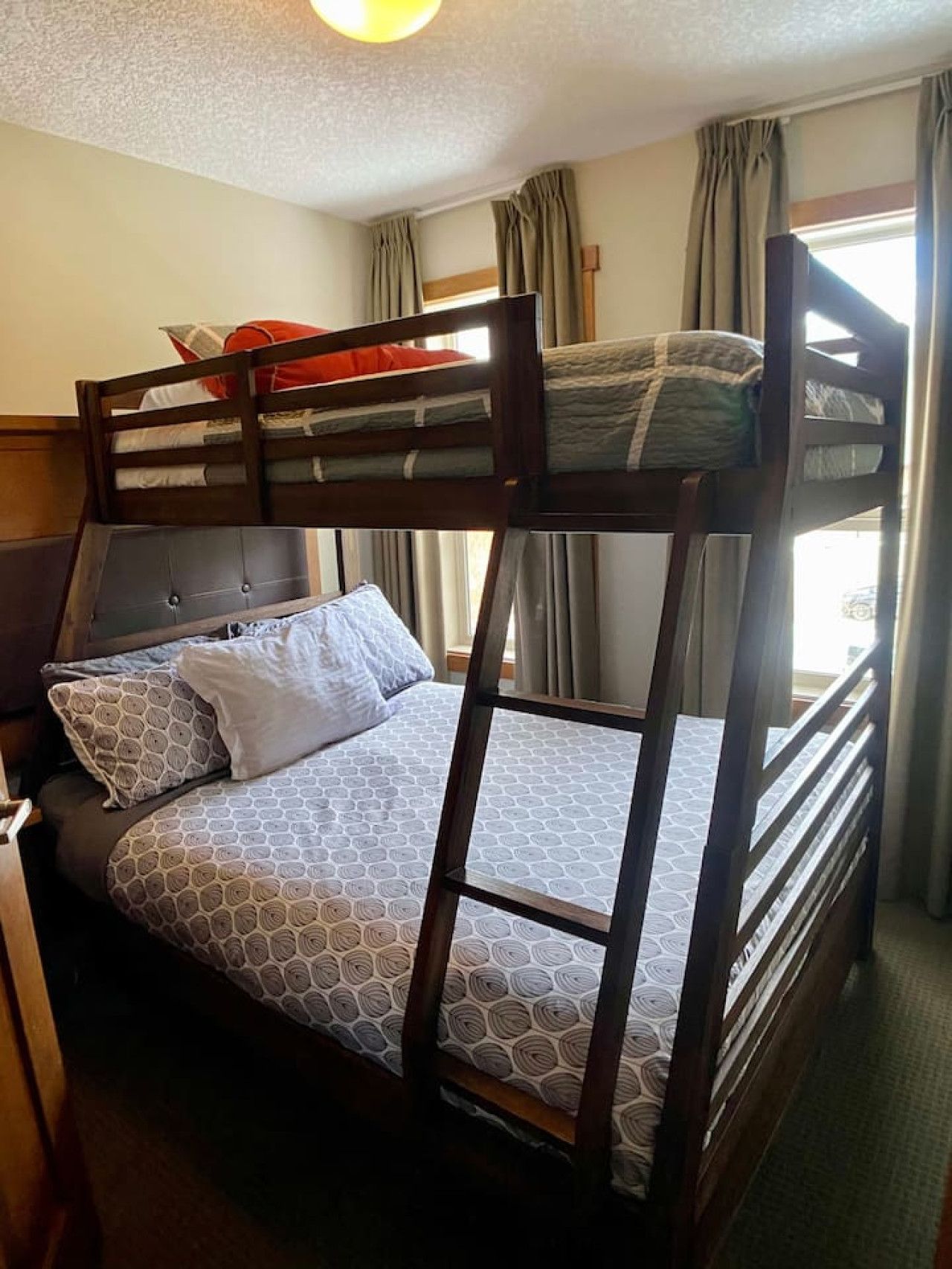 Ein Etagenbett mit Kopfteil, ein Unterbett mit gemusterten Betttextilien und ein Fenster mit Vorhängen.