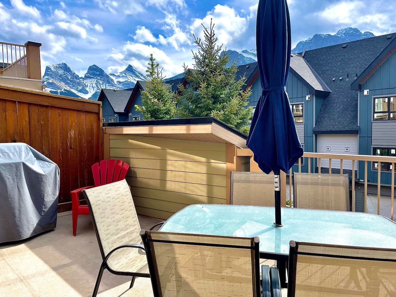 A patio with a table and chairs, a covered grill, and a view of mountains.