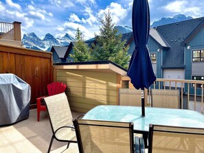 Une terrasse avec une table et des chaises, un barbecue abrité et une vue sur les montagnes.