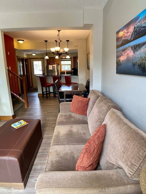 A living room with a sofa, a coffee table, and a painting on the wall. - 212 Canmore Chalet With Beautiful Mountain Views (Canmore)