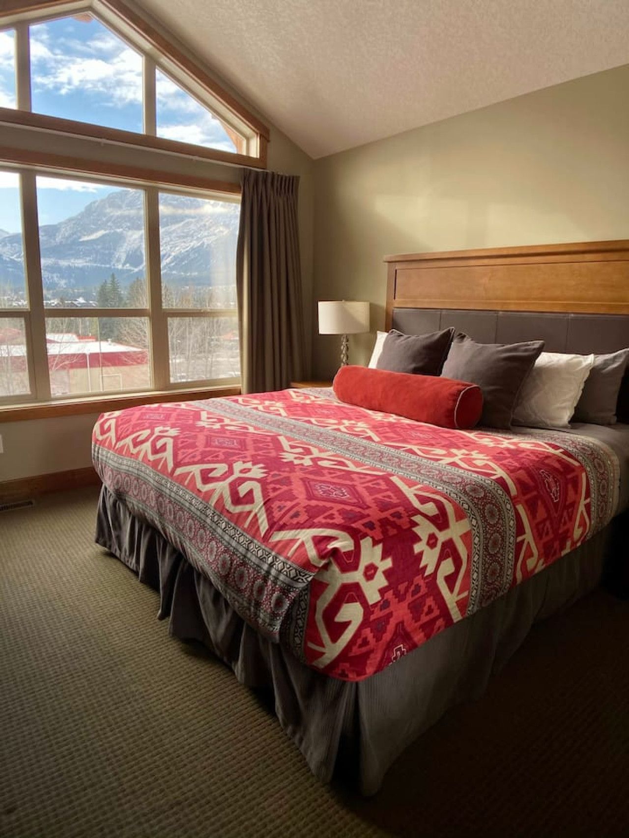 A hotel room with a large bed, a view of mountains, and a window with curtains.