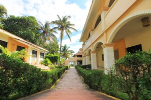 Un camino que lleva a un edificio con varios balcones y una palmera al fondo.