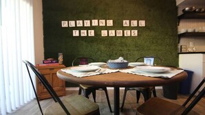 Un'area pranzo con un tavolo rotondo apparecchiato per quattro persone, una parete verde decorata con un motivo a tema gioco e una finestra con persiane.