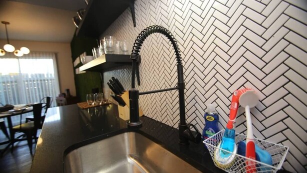 Una cucina con lavello in acciaio inossidabile, zoccolo posteriore a motivi a spina di pesce e porta utensili.