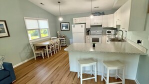 Een moderne keuken met witte apparaten, een eethoek met een tafel en stoelen, en een groot raam.