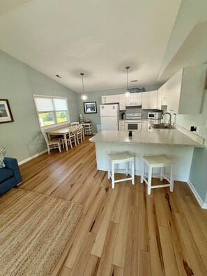 A modern kitchen with white appliances, a dining area with a table and chairs, and a large window. - Middle of the Row Duplex, Quiet, and Cozy, 3 bed/2 bath (Emerald Isle)