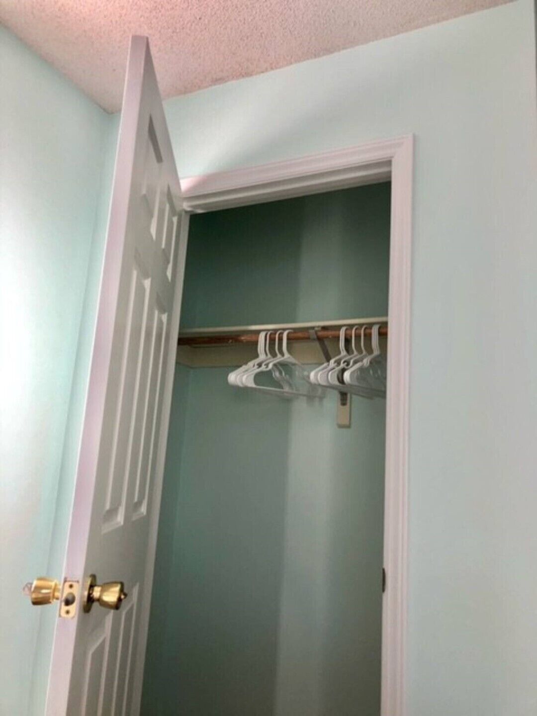 A room with a light blue wall, a white door with a brass doorknob, and a coat rack with several hangers.