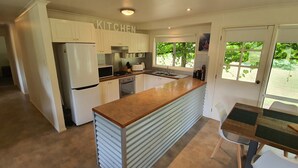 A modern kitchen with white cabinetry, a built-in oven, a refrigerator, and a window providing a view of greenery outside. - Feathertop Views and Barn (Smoko)