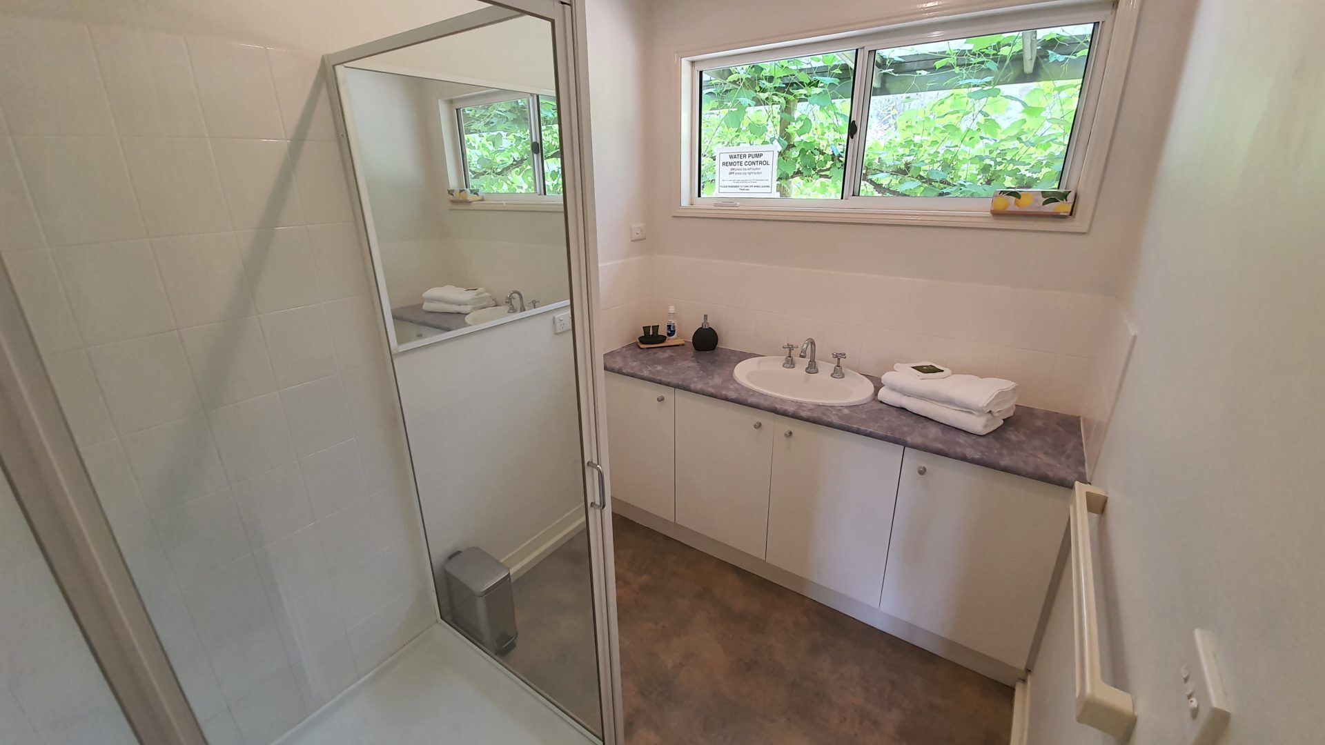 Ein Badezimmer mit Dusche, zwei Waschbecken, einem Fenster mit Blick auf Grünflächen und einem Spiegel.