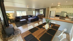 A modern living room with a sectional sofa, a dining table with placemats, and a kitchen area with white cabinets and appliances. - Feathertop Views and Barn (Smoko)