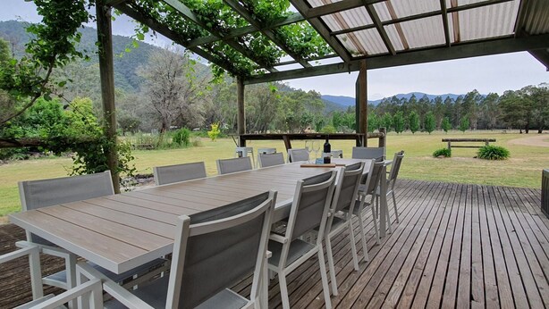 An outdoor patio with a wooden table and chairs, surrounded by a wooden deck and a pergola. - Feathertop Views and Barn (Smoko)