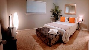 A bedroom with a bed, a nightstand, a lamp, a potted plant, and a mirror. - North Austin Hip Duplex (Austin)
