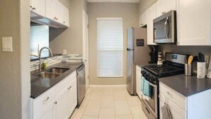 A compact kitchen with white cabinets, a black countertop, a stainless steel sink, a stove, and a refrigerator. - North Austin Hip Duplex (Austin)