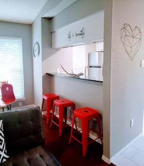A modern kitchen with a white countertop, three red stools, and a wall with a geometric heart design. - North Austin Hip Duplex (Austin)