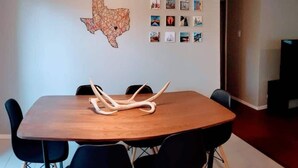 A dining area with a wooden table, black chairs, a decorative antler centerpiece, pendant lights, and a wall with a Texas map and framed photos. - North Austin Hip Duplex (Austin)