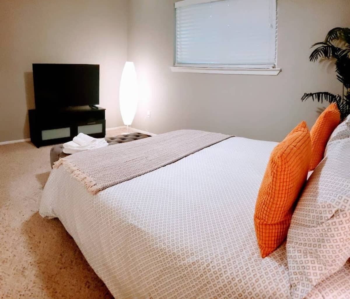 A bedroom with a bed, a TV, a lamp, and a window.