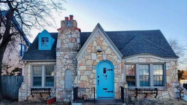 Ein Steinhaus mit blauer Tür, einer kleinen angebauten Garage und einem Steinkamin.