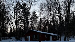 A snow-covered landscape with a single red cabin surrounded by trees. - Killington / Rutland 1 Bdroom Cabin, Cabin #1 (Mendon)
