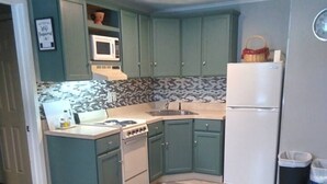 A compact kitchen with teal cabinets, a white refrigerator, a microwave, a stove, and a tiled backsplash. - Killington / Rutland 1 Bdroom Cabin, Cabin #1 (Mendon)